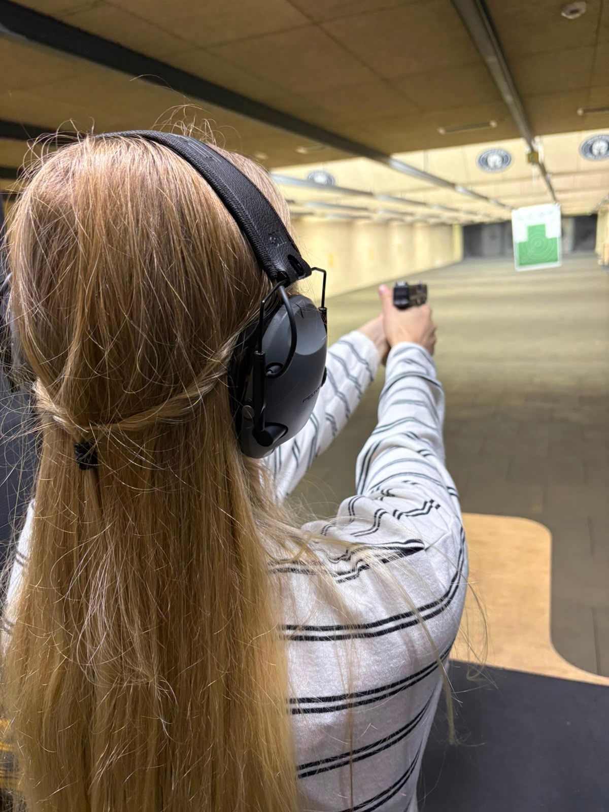 A visitor in ear defenders aims at a target on the firing line, seen from behind
