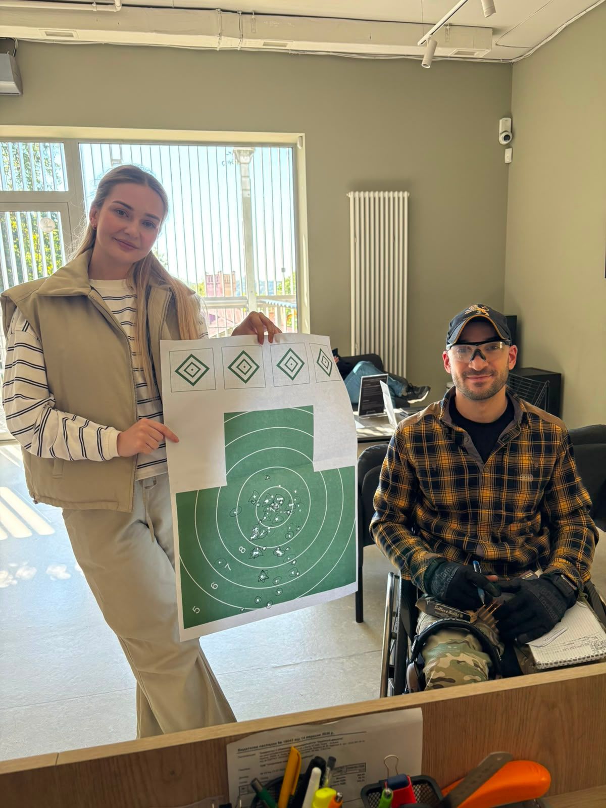 A visitor holds up her first target next to a smiling instructor